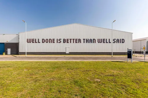 Photo of a building facade in Rotterdam's Keile District. The wall shows a saying: "Well done is better than well said."