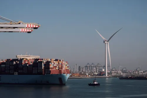 The port of Rotterdam lined with windmills, vessels with shipping containers on the water.