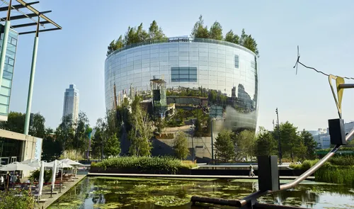 Exterior view of Depot Boijmans Van Beuningen in Rotterdam, a modern mirrored building with trees on the roof and a reflection of the surrounding cityscape.