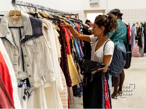 A woman browsing a rack of vintage clothing, whilst holding a couple of clothing items to try on.