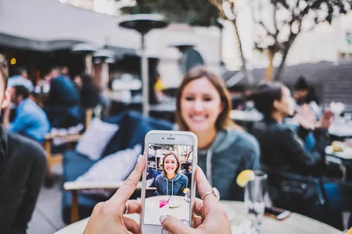 Photo of someone taking a picture with a phone, of a woman sitting across a table