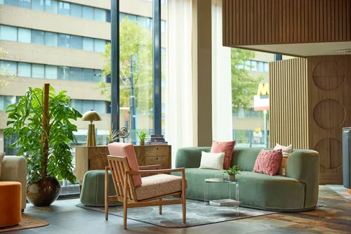 Modern hotel lounge at Hilton Curio Collection in Rotterdam, featuring soft green and blush tones, large windows, and mid-century inspired furniture.