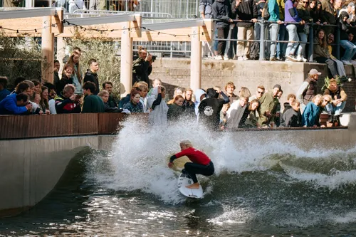 Photo of a person surfing at Rif010, Rotterdam's spectacular innercity surf pool. Lots of people looking on.