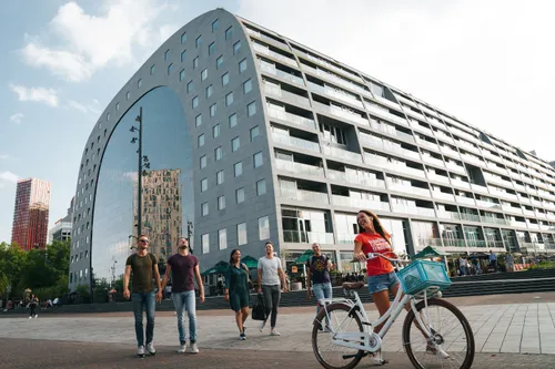 Rotterdam’s Markthal: people walking and a cyclist in front of the iconic arch-shaped building housing a market and apartments.