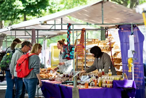 A woman selling trinkets and hand-made goods at a market stall to two customers.