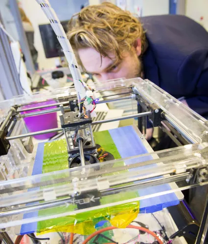 Photo of a young man examining a 3D printer at work