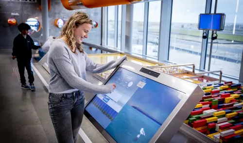 Interactive touchscreen kiosk at PortLantis Rotterdam visitor center with shipping container model and port crane views.