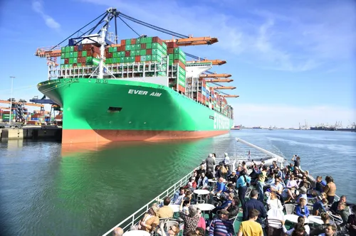 Bezoekers op een rondvaartboot varen langs een groot containerschip in de haven van Rotterdam