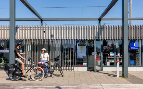 Moderne VVV-kiosk aan de boulevard van Hoek van Holland waar twee fietsers met helm in gesprek zijn, klaar om de omgeving te verkennen.