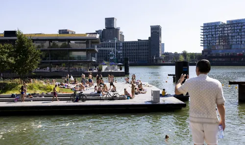 Een foto van een man die een foto maakt van zwemmers en het Floating Office in de Rijnhaven