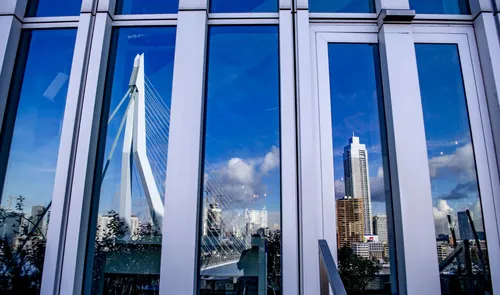 Een foto van de facade met ruiten van De Rotterdam met een weerspiegeling van de Erasmusbrug