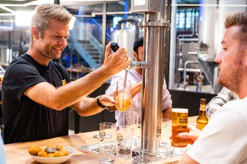 Guest pouring fresh Stadshaven beer from a tap tower at the table while another guests enjoy drinks and snacks at the brewery bar.