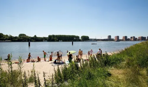 Bezoekers genieten van een zomerse dag op het strand aan de Maas bij De Esch in Rotterdam
