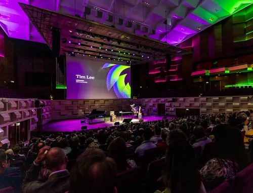 Photo of Tim Lee addressing the audience at InnovationQuarter's year event 2025. Photo taken from behind the audience, looking towards the stage.