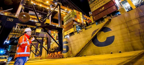 Photo of a man checking a cargo ship at night in the port of Rotterdam. He is standing on the quay.