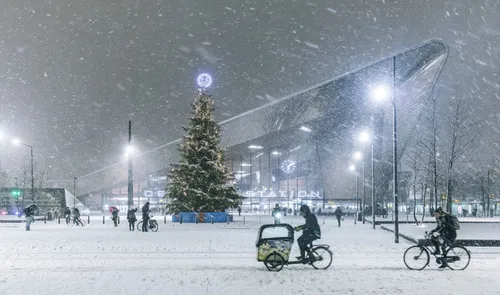 Fietsers in de sneeuw met op de achtergrond Rotterdam Centraal Station met de kerstboom