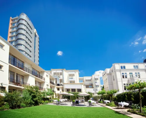 Elegant exterior of Bilderberg Parkhotel Rotterdam, featuring a lush garden terrace and white façades, set against a clear blue sky.