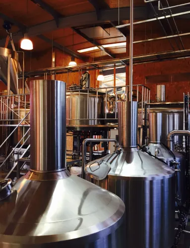 Interior of Brouwerij Noordt featuring large stainless steel brewing tanks and industrial piping under warm ambient lighting.