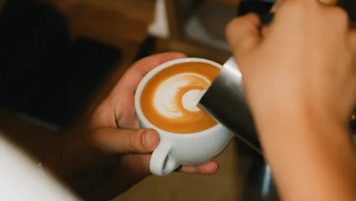 A barista pouring latte art into a coffee cup.