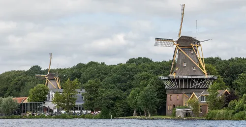 Twee historische windmolens aan het water bij Rotterdam, omringd door groen.
