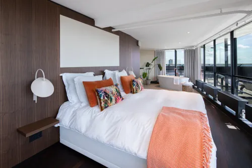 Euromast suite bedroom with king-size bed and freestanding bathtub overlooking the Rotterdam skyline.