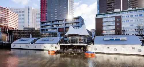 Floats byH2Otel in Rotterdam, with modern houseboats moored along the water and city buildings in the background.