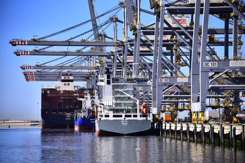 Photo: Ship moored at a quay in Rotterdam's port. Cranes and containers visible.
