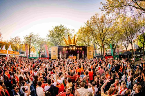 Feestelijke Koningsdagviering op het Noordplein in Rotterdam, met een groot dansend publiek en een podium met kroon.