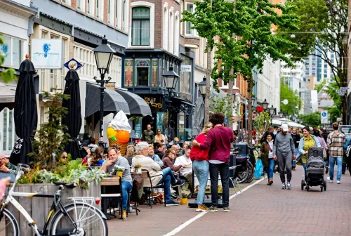 Shoppers strolling on the Oude Binnenweg street, past a full café terrace.