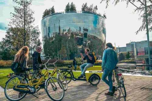 A photo of a guide sitting on a cargo bike in front of Depot Boijmans Van Beuningen talking to three other bikers.