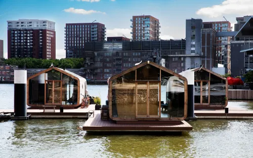 Floating tiny house cabins on the water in Rotterdam, with modern wooden design and the city skyline in the background.